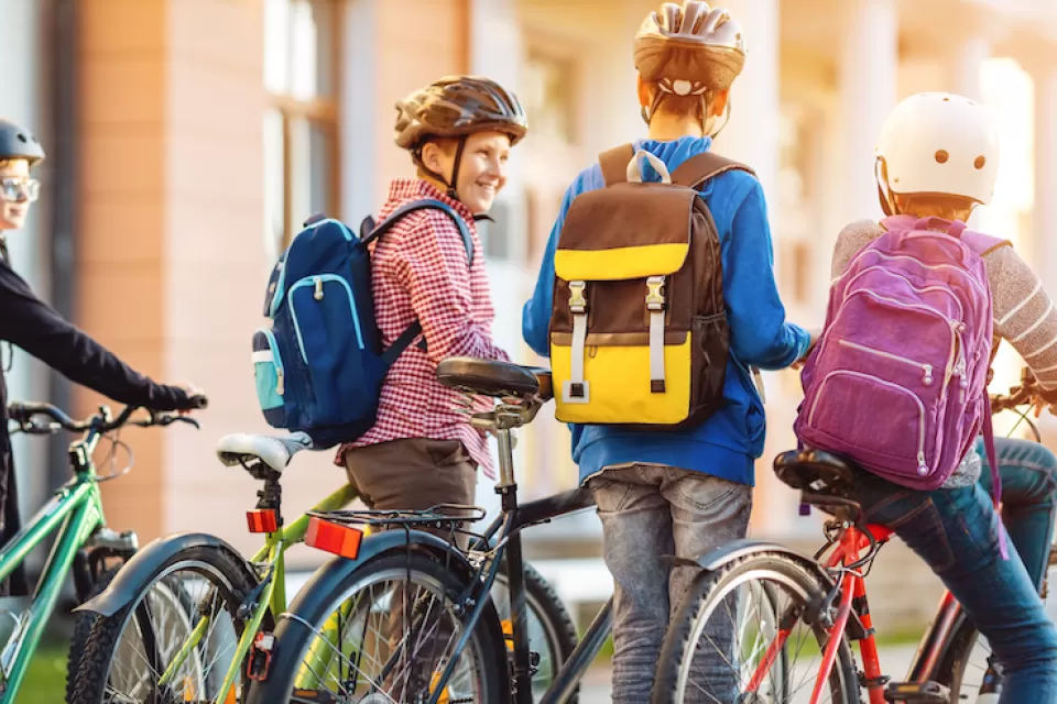 Group of four children with backpacks and helmets riding and walking their bikes.